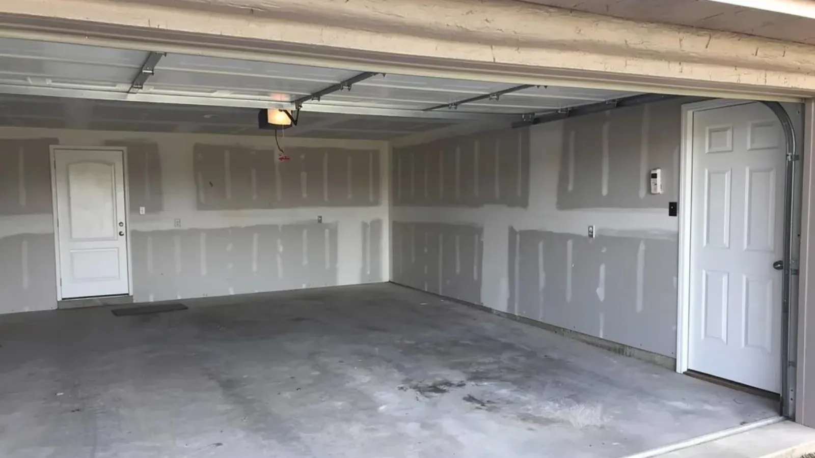 Attached garage with the walls and ceiling drywalled and taped, seen through the open overhead door