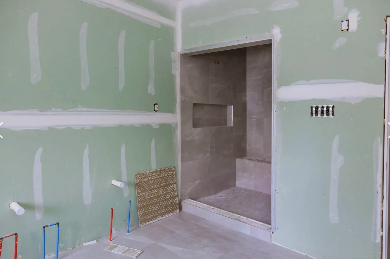 Bathroom framed in green moisture-resistant drywall around a tiled walk-in shower with a recessed niche, plumbing stubbed out and rough openings cut for fixtures